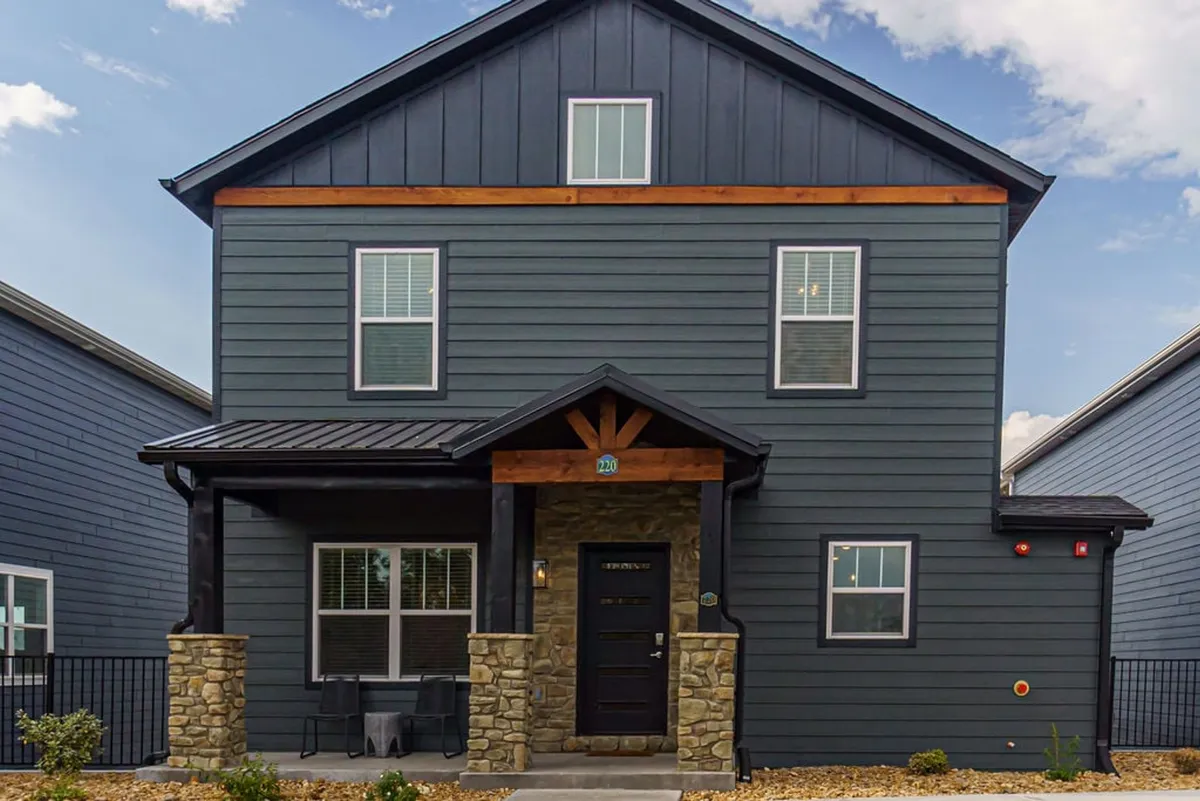 An exterior view of the home's stone facade and welcoming front door, framed by a roof overhang and a porch with comfortable seating. The setting is ideal for gatherings and enjoying the outdoors, with the porch offering a seamless transition between indoor and outdoor living.