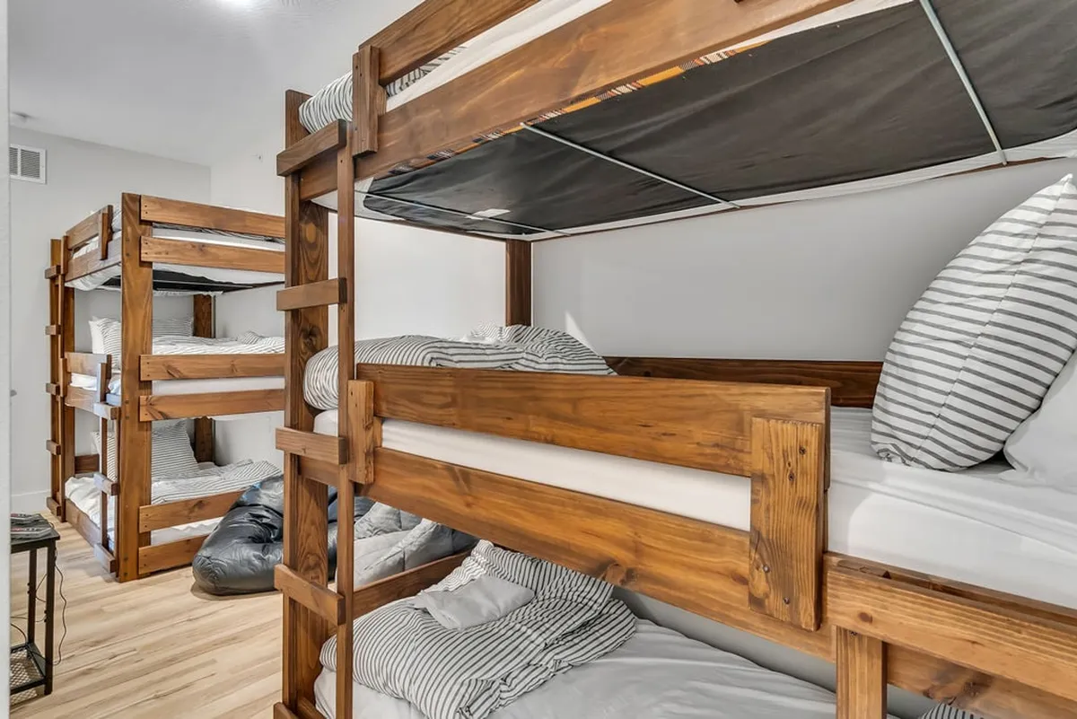 This image showcases a cheerful bunk room with multiple bunk beds featuring striped bedding, ample floor space, and bright, natural light. The playful setup is ideal for kids or groups and evokes a sense of fun and togetherness, perfect for sleepovers or late-night storytelling.