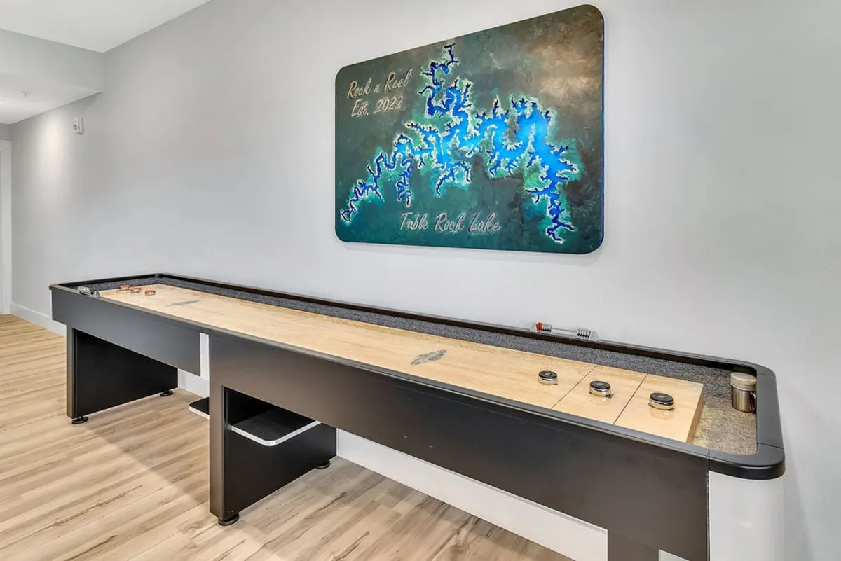 This image centers on a shuffleboard table set against a stylish wall with modern artwork, capturing the playful and social vibe of a game room. The setting is open and inviting, suggestive of friendly competitions and group fun.