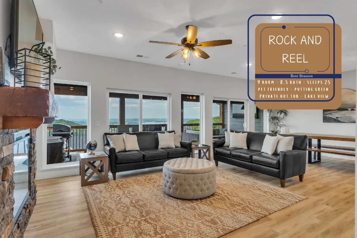 This inviting living space includes comfortable black sofas arranged around a large round ottoman, all facing expansive windows with stunning lake views. The room is designed for relaxation and socializing, with plenty of natural light and cozy seating for gatherings. The connection to the outdoors is clear through the panoramic windows.