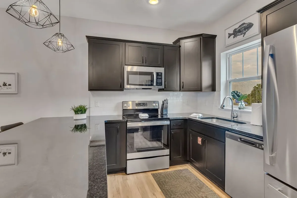 A modern kitchen is showcased here, complete with dark cabinetry, stainless steel appliances, a spacious island counter, and elegant pendant lighting overhead. The layout is open, inviting, and ready for cooking or entertaining, with a stylish and functional vibe that fits the narrative of culinary adventures.