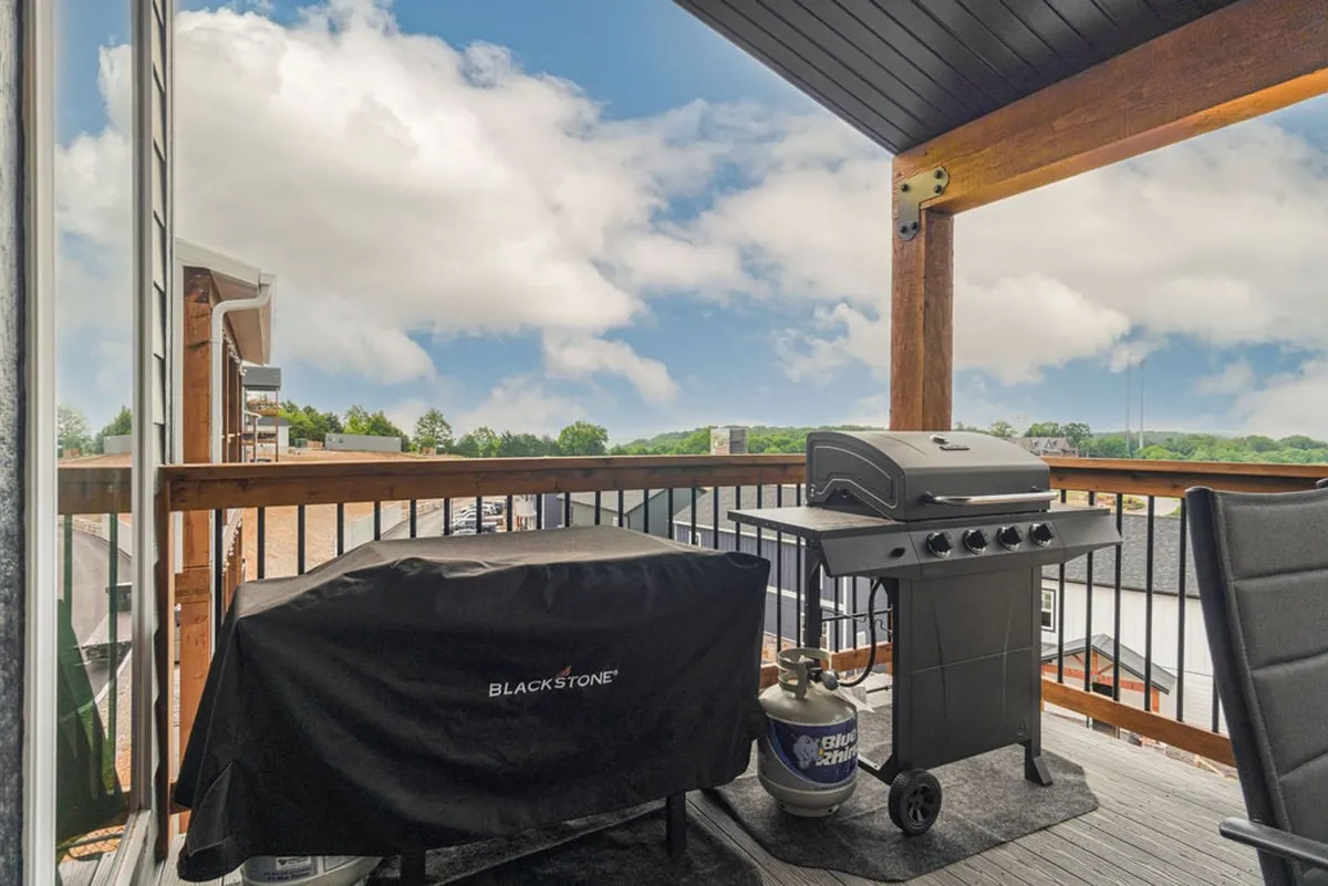 A view of the balcony featuring a grill, outdoor chairs, and a sturdy railing, set against an open sky. The atmosphere is casual and inviting, perfect for morning coffee, sunset barbecues, or simply lounging outdoors with a pet.